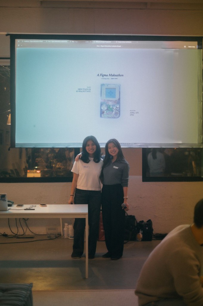 Two people in front of a screen showing a Figma Makeathon presentation.