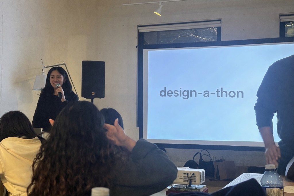 Speaking at a design-a-thon in front of a projected presentation screen.